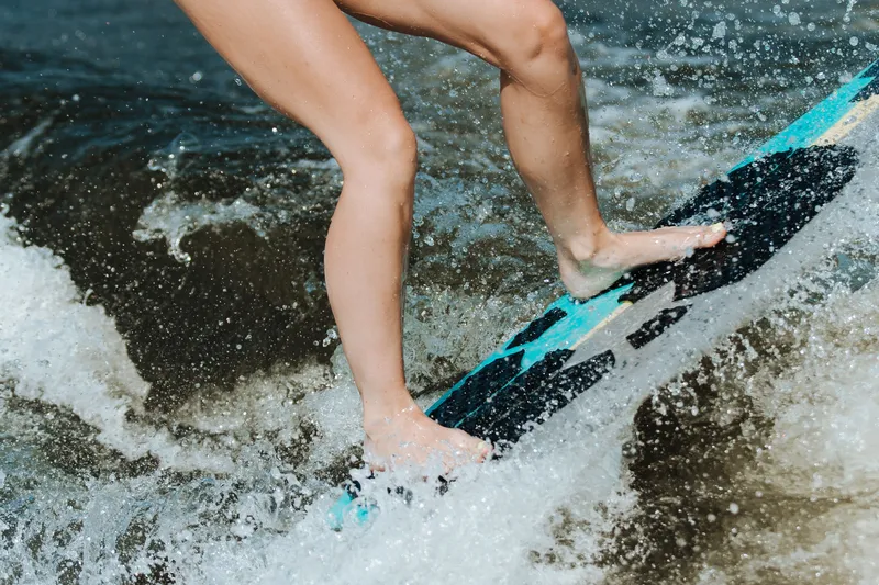 Bare feet holding a surfboard through the spray